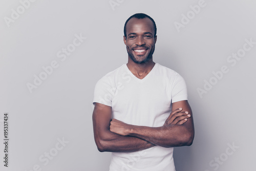Portrait of sexy, smiling, brutal, stunning, trendy man with black skin in white t-shirt having his arms crossed, looking at camera, isolated on grey background