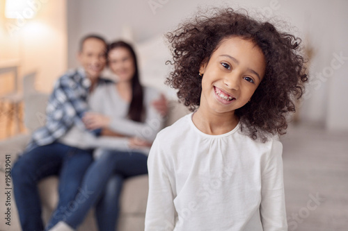 Happy life. Nice alert curly-haired girl smiling and her sitting on the couch and hugging in the background