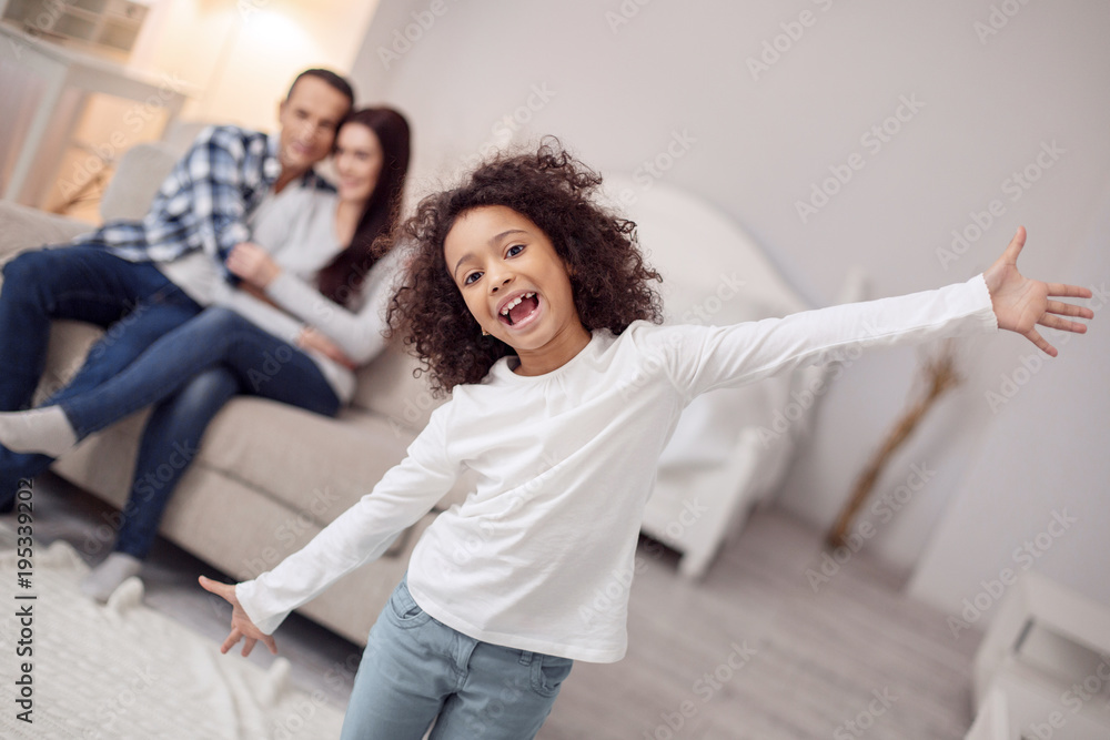 Relaxation. Beautiful alert curly-haired girl smiling and spreading her arms and her sitting on the couch in the background Relaxation. Beautiful alert curly-haired girl smiling and spreading her arms and her sitting on the couch in the background