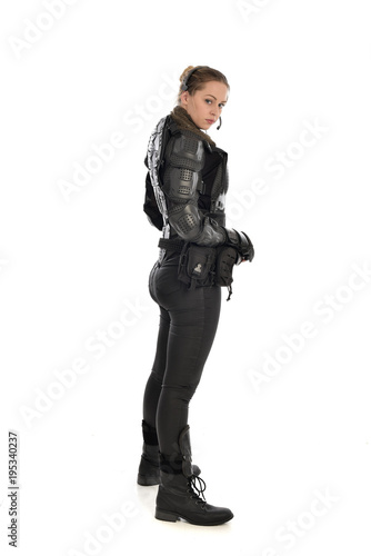 full length portrait of female soldier wearing black tactical armour, standing in side profile, isolated on white studio background.