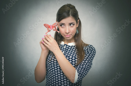 Happy merry unconcern woman holding in hand a toy red butterfly and is amazed. Innocent excited girl concept. Carefree bahavior. Dreaming girl.