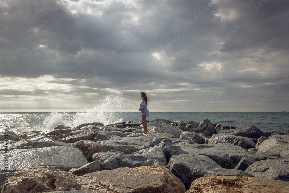 portrait of young woman standing on stony sea shore during stormy sunrise