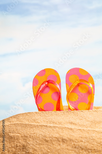 Summertime Season, colorful spotty sandals or flip-flop on the sandy beach with sunny colorful blue sky background and copy space. Traveling and feeling lonely, cheering up, rest, refresh and relax