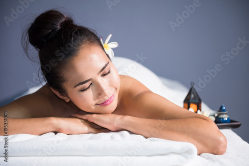 portrait of young happy Asian beautiful woman relax in spa. Body care treatment. Cute girl having massage at back by professional massager hands with candle and white Plumeria on bed.