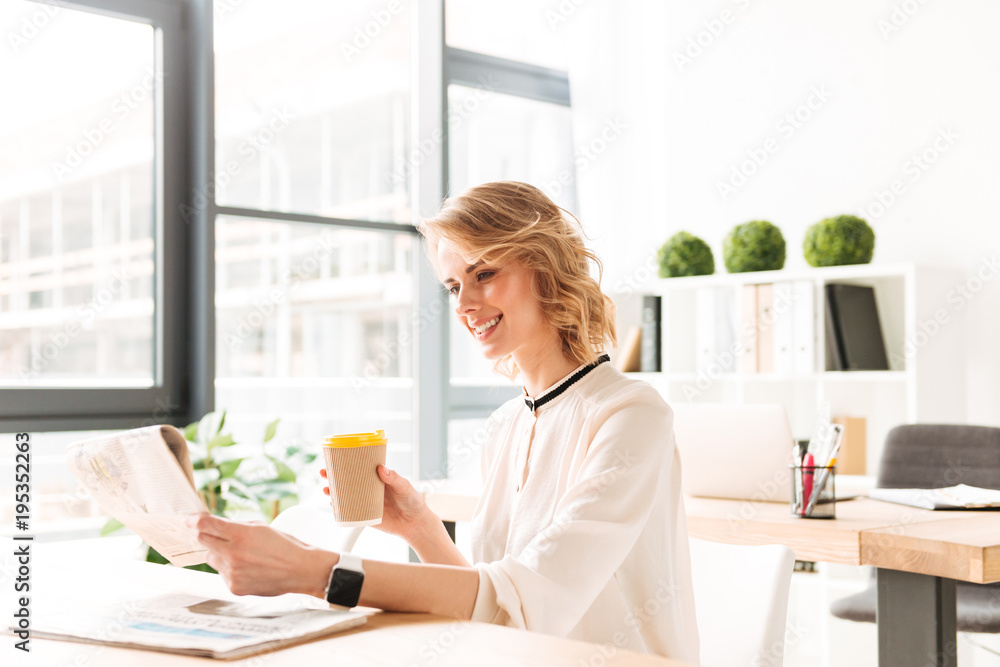 Smiling young business woman reading newspaper drinking coffee. Smiling young business woman reading newspaper drinking coffee.