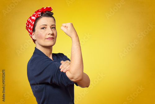 Fototapeta Self-confident middle aged woman with a clenched fist rolling up her sleeve, tex