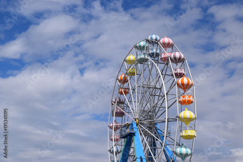 Colorful ferris wheel against sunny blue sky with clouds.