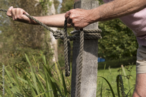 Mooring line being held in man's hands being attached to a post with a round turn and two half hitches knot © petert2