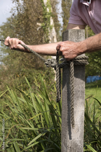 Mooring line being held in man's hands being attached to a post with a round turn and two half hitches knot