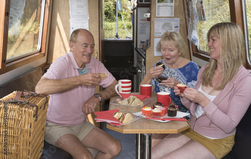 Billede på lærred Holidaymakers enjoying afternoon tea of sandwiches and cakes aboard a narrowboat