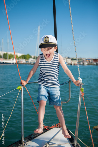 funny cute little boy in captain's hat on a yacht in the seaport in summer cruise