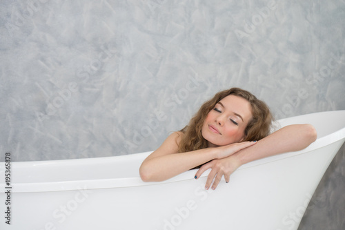 Caucasian woman laying and closing eyes in bathtub. Girl in bathtub relaxing smiling.