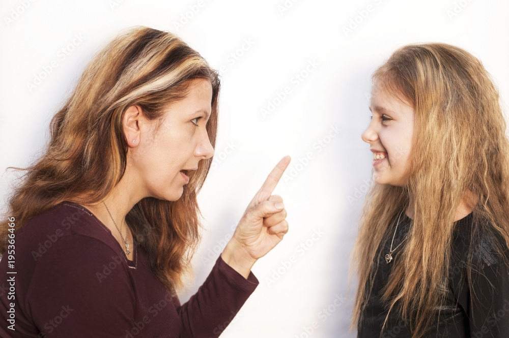 Mom scolding her daughter with an angry face and waves her finger on a white background. Daughter at the same time just smiles Mom scolding her daughter with an angry face and waves her finger on a white background. Daughter at the same time just smiles