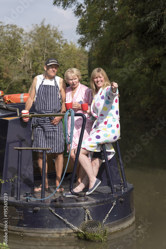 Three holidaymakers traveling on a narrowboat early morning. Holding mugs and women wearing dressing gowns