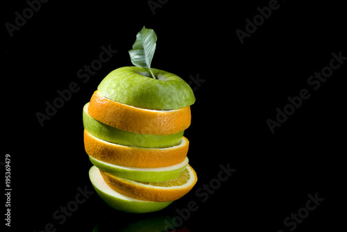 Slices of green apple and orange stacked in a pile on a black background.