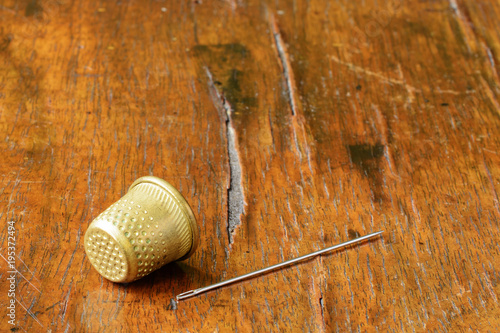 Thimble and a needle on an antique wood veneer full of cracks and scratches. Selective focus. Closeup. There is a lot of copy space in the photograph. 