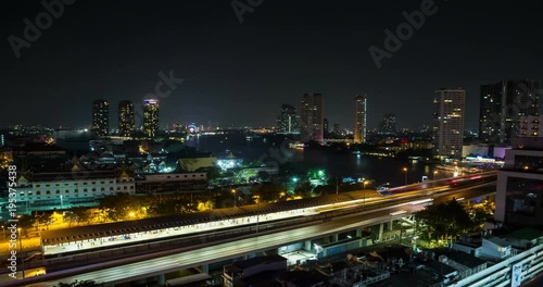 Cityscape time lapse of Bangkok at night featuring skytrain station and river transportation.