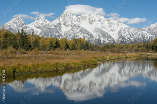 Autumn colored trees and snowy mountains reflecting in the water