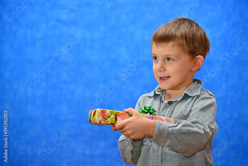 A boy with a gift in his hands in the studio with an open mouth on a blue background looking out into the distance photo