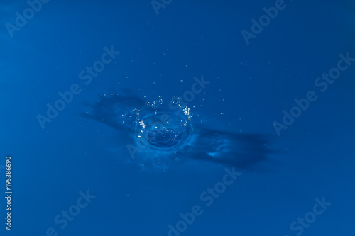 drop of water liquid with splash isolated. the drop explodes in the water sending spray to the sides and circle ripples around it. the water is blue