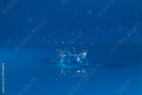 drop of water liquid with splash isolated. the drop explodes in the water sending spray to the sides and circle ripples around it. the water is blue