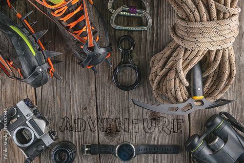 Top view of rock climbing equipment on wooden background. Chalk bag, rope, climbing shoes, belay/rappel device, carabiner and ascender. Active lifestyle concept.