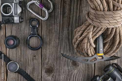 Top view of rock climbing equipment on wooden background. Chalk bag, rope, climbing shoes, belay/rappel device, carabiner and ascender. Active lifestyle concept.