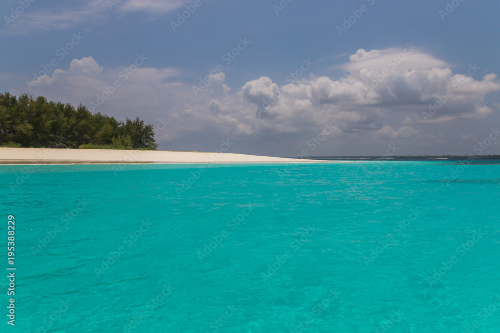Turquoise water blue sky on a tropical island. The sand is white and the water is calm and there are clouds in the sky. The water is crystal clear. There are green trees on the island .Zanzibar Turquoise water blue sky on a tropical island. The sand is white and the water is calm and there are clouds in the sky. The water is crystal clear. There are green trees on the island .Zanzibar
