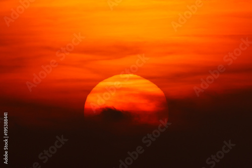 red big sun obscured by clouds near the horizon at sunset or sunrise. The sun is partially seen through the clouds 