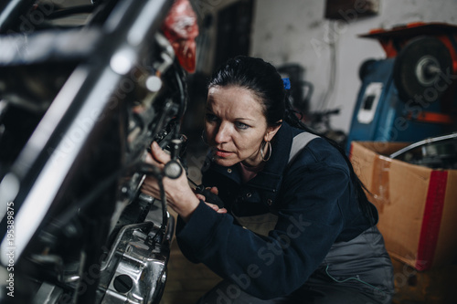 Strong and worthy woman doing hard job in car and motorcycle repair shop. © Dusko