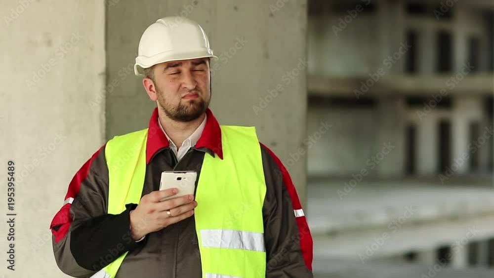 Builder in green vest with cell phone on project site. Workman in white helmet with smartphone on construction site Builder in green vest with cell phone on project site. Workman in white helmet with smartphone on construction site