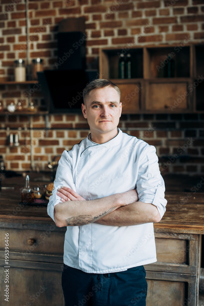 Fototapeta premium Portrait of a chef in the uniform standing near a table in the kitchen