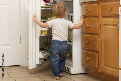 Two years blonde toddler openes fridge and lookes what to eat