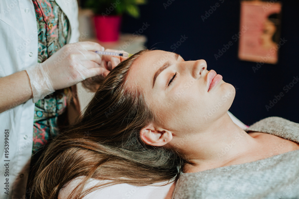Naklejka premium Woman in cosmetology cabinet. Cosmetologist is doing injection. woman receives an injection in the head. The concept of mesotherapy. 