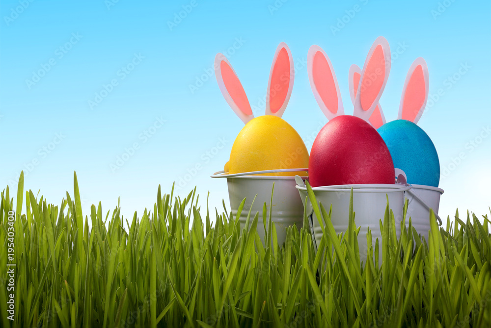 Fototapeta premium Colorful easter eggs with bunny ears in green grass on background. Holidays background.Easter greeting cards
