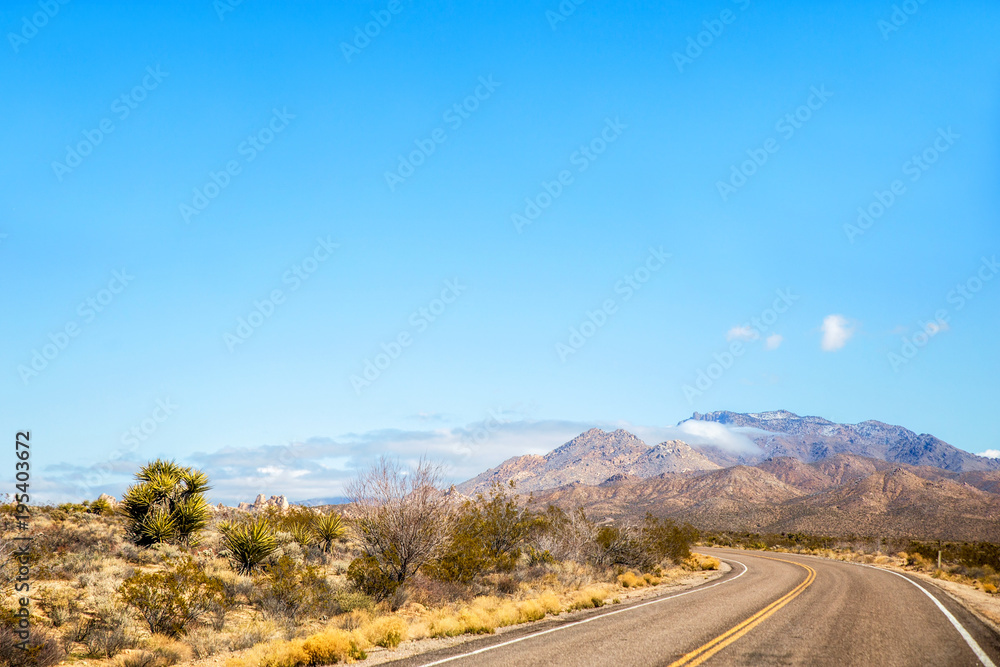 A highway cutting through the Mojave desert with a large mountain in the foreground in a march landscape