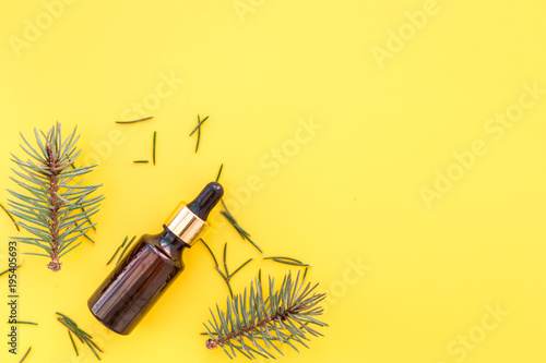 Pine essential oil in bottles on yellow background top view. Pattern with pine branch and cone copy space
