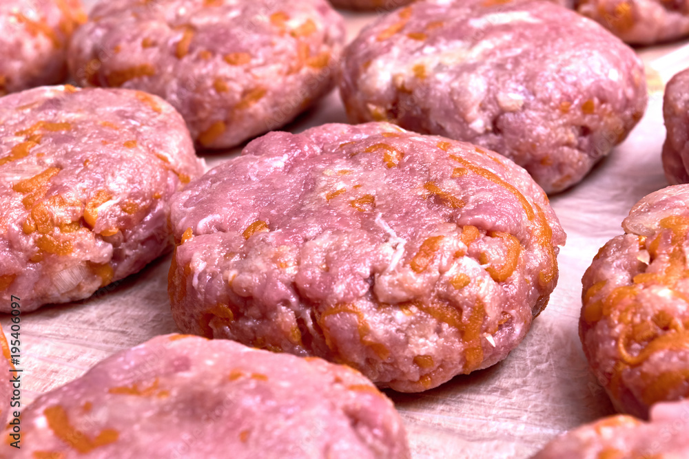 Fresh cutlets of beef and pork lie on a wooden Board covered with a film. Cutlets lie in several rows and lines. Carrots, onions and garlic are added to minced meat. The meatballs are homemade.