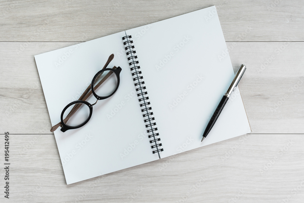Opening white blank paper note book with pen on the right and glasses on the left on light grey wooden table background with copy space Opening white blank paper note book with pen on the right and glasses on the left on light grey wooden table background with copy space