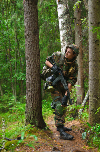 soldier with a rifle carefully and stealthily goes through the woods between the trunks of the trees