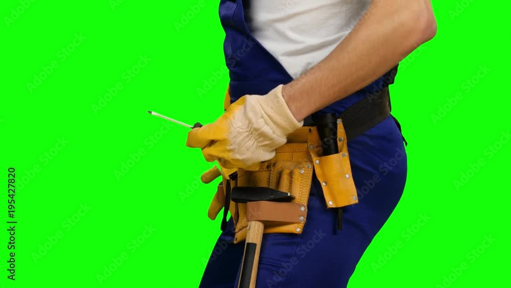 Worker takes out a screwdriver from his construction belt. Green screen. Side view. Close up Worker takes out a screwdriver from his construction belt. Green screen. Side view. Close up