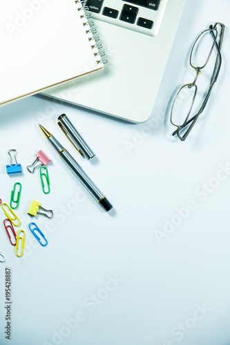 Top view of laptop, blank notebook, paper clips and smart phone with white background and copy space.