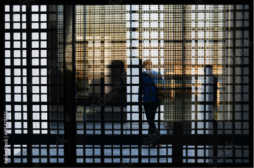 A person refects in the many interesting surfaces, against grid covered windows.