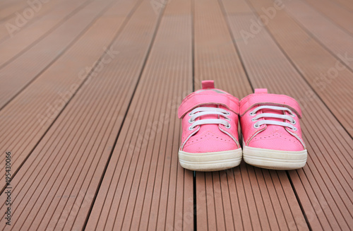 Pair of pink baby leather sneakers on wood plank background.