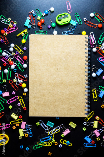 Top view of office table or desk with blank notebook and colorful equipment on black background with copy space for text.
