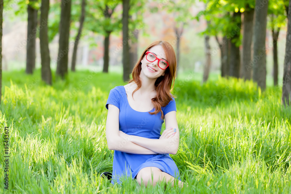 redhead girl in eyeglasses sitting on green grass redhead girl in eyeglasses sitting on green grass