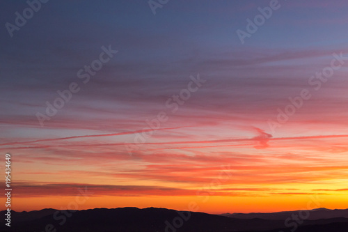 Clouds and jet vapor trails creating beautiful, colorful texture in the sky at sunset with mountain profiles on the low part of the frame © Massimo