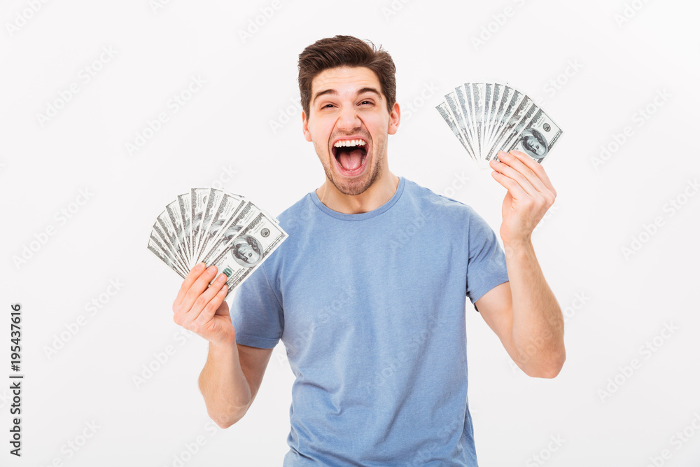 Photo of ecstatic man in casual t-shirt screaming and rejoicing his money prize in cash, isolated over white wall Photo of ecstatic man in casual t-shirt screaming and rejoicing his money prize in cash, isolated over white wall