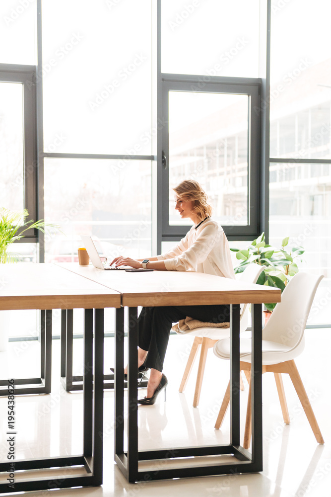 Happy young business woman sitting in office using laptop Happy young business woman sitting in office using laptop