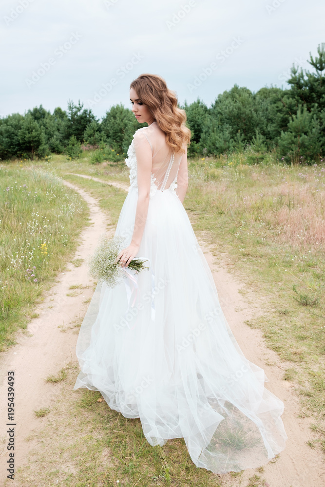 bride in white llight wedding dress with bridal bouquet walking in lane, back view bride in white llight wedding dress with bridal bouquet walking in lane, back view